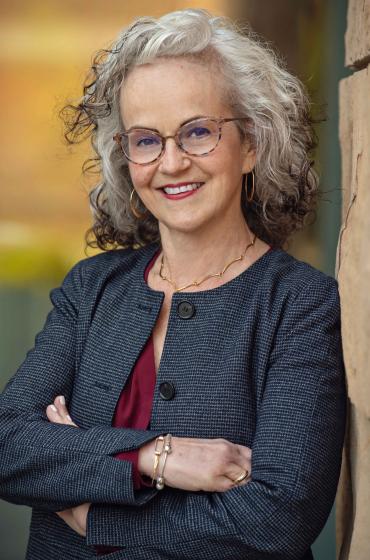 Photo of Deborah Loewenberg Ball with her arms crossed, leaning against a brick wall