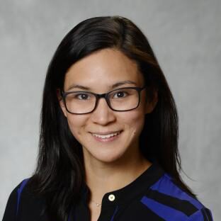 Headshot, with long dark hair, wearing glasses and smiling, wearing a purple and black top.