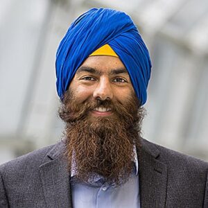 Headshot wearing a beard, suit and collard shirt and blue and yellow head covering.