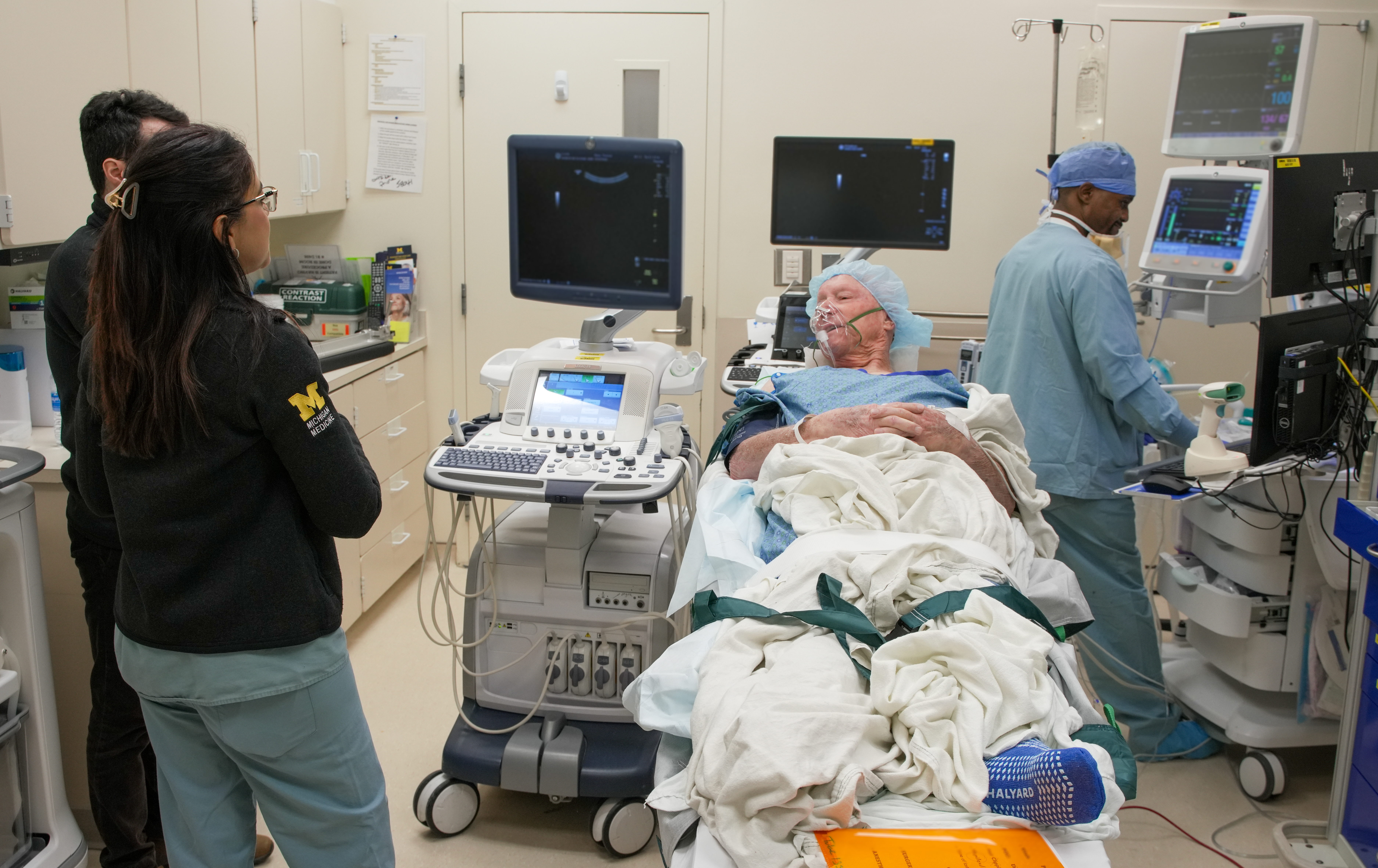 DSC00012 photo of a patient in a hospital bed, wearing a cap and scrubs, speaking with medical staff in a hospital room