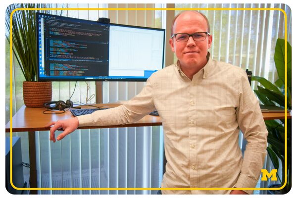 impact stories - web buttons (5) photo of Michael Sjoding standing next to his computer showing a coding screen