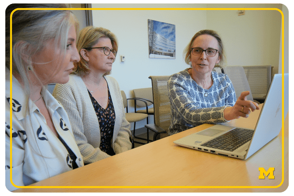 impact stories - web buttons (6) photo of three women talking at a conference table and working on a laptop