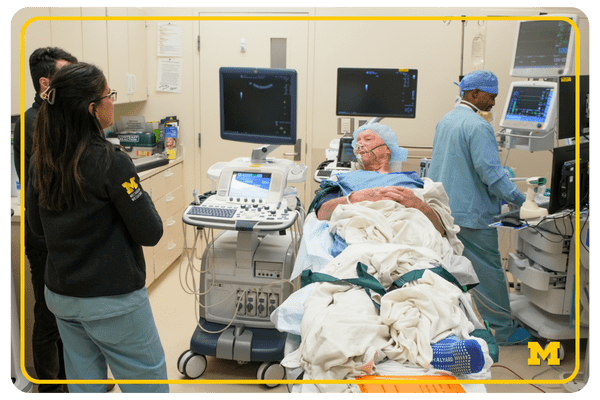 impact stories - web buttons (7) photo of a patient in a hospital bed, wearing a cap and scrubs, speaking with medical staff in a hospital room