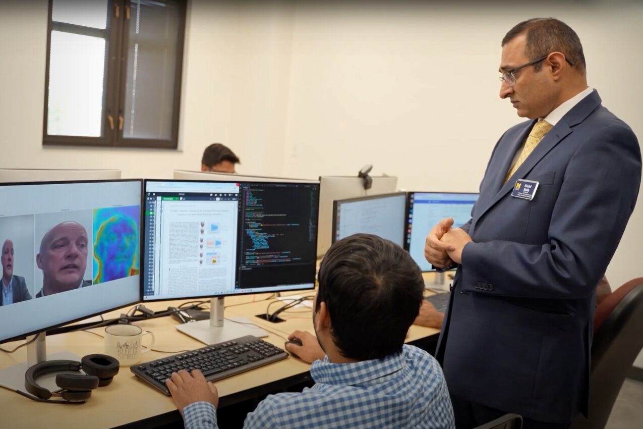 Professor Khalid Malik stands next to a research working at a computer on a deepfake detection tool