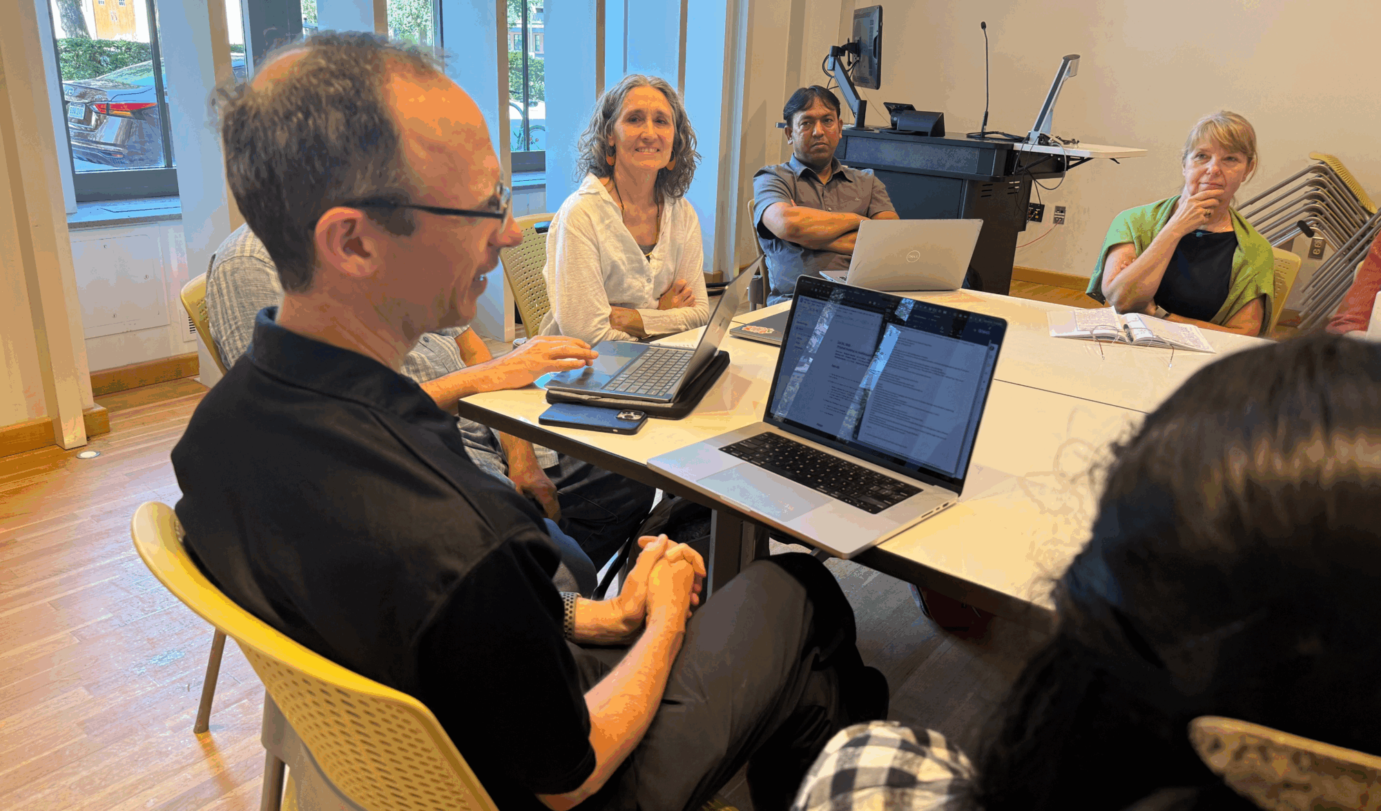Dr. Christi Merrill and her colleagues Group of people sit in a classroom around tables with laptops, engaged in active discussion and collaborative work