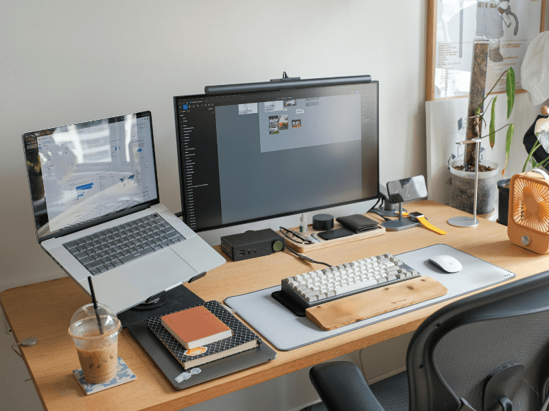 Image of a typical desk with laptop, monitor, coffee cup, and work documents on it.