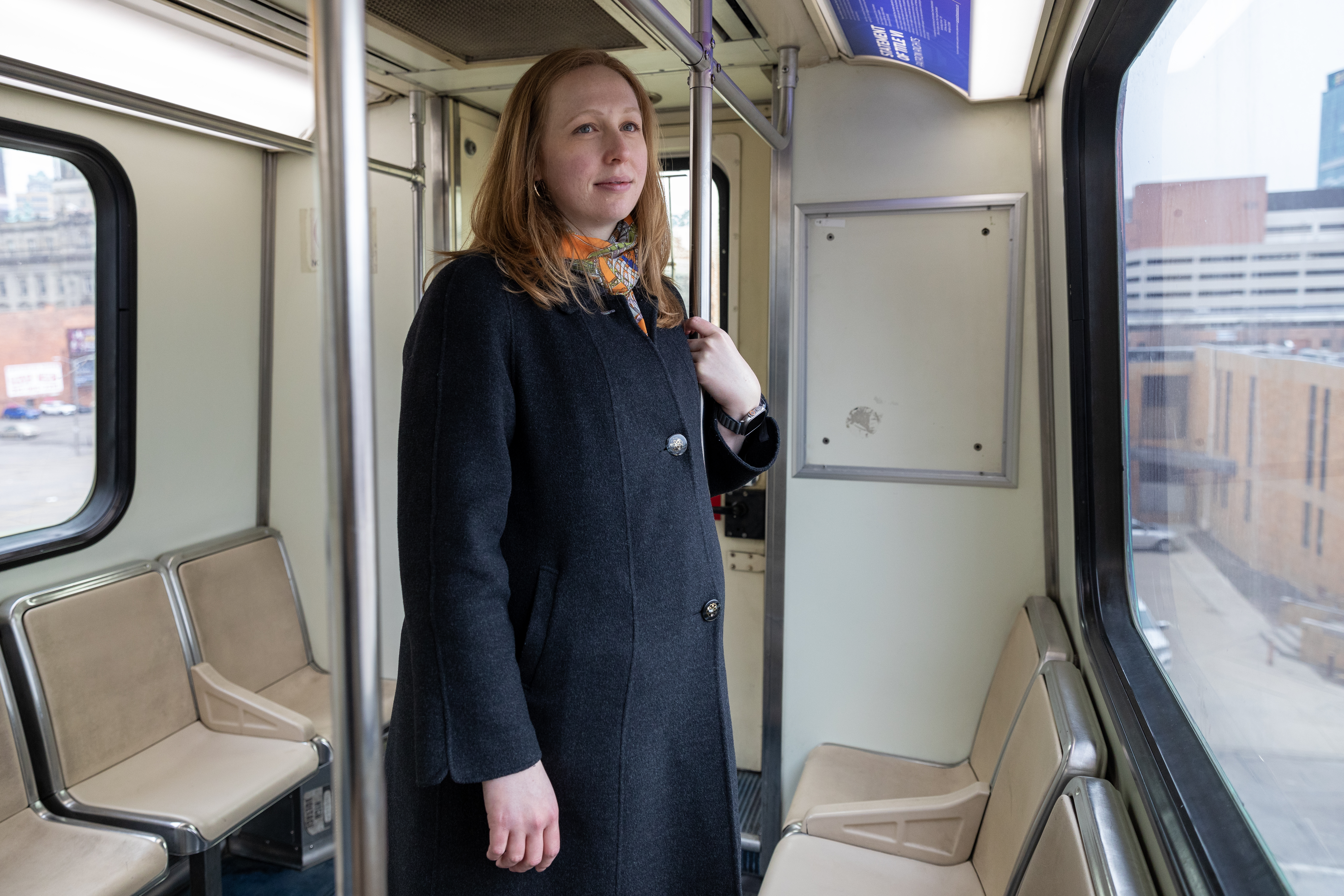 Erica Twardzik stands on a bus looking out the window at the city.