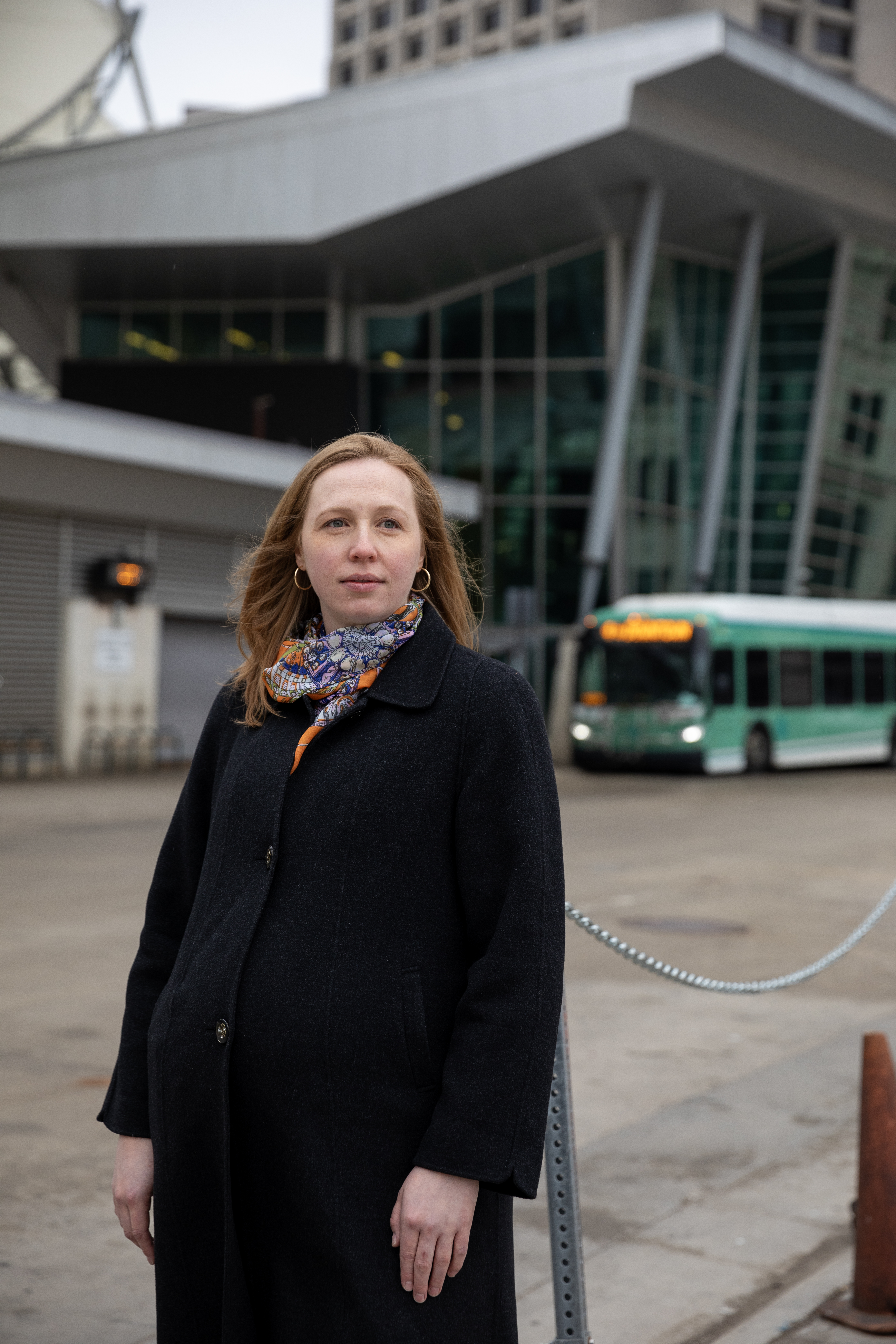 Erica Twardzik stands looking on in front of a bus station.