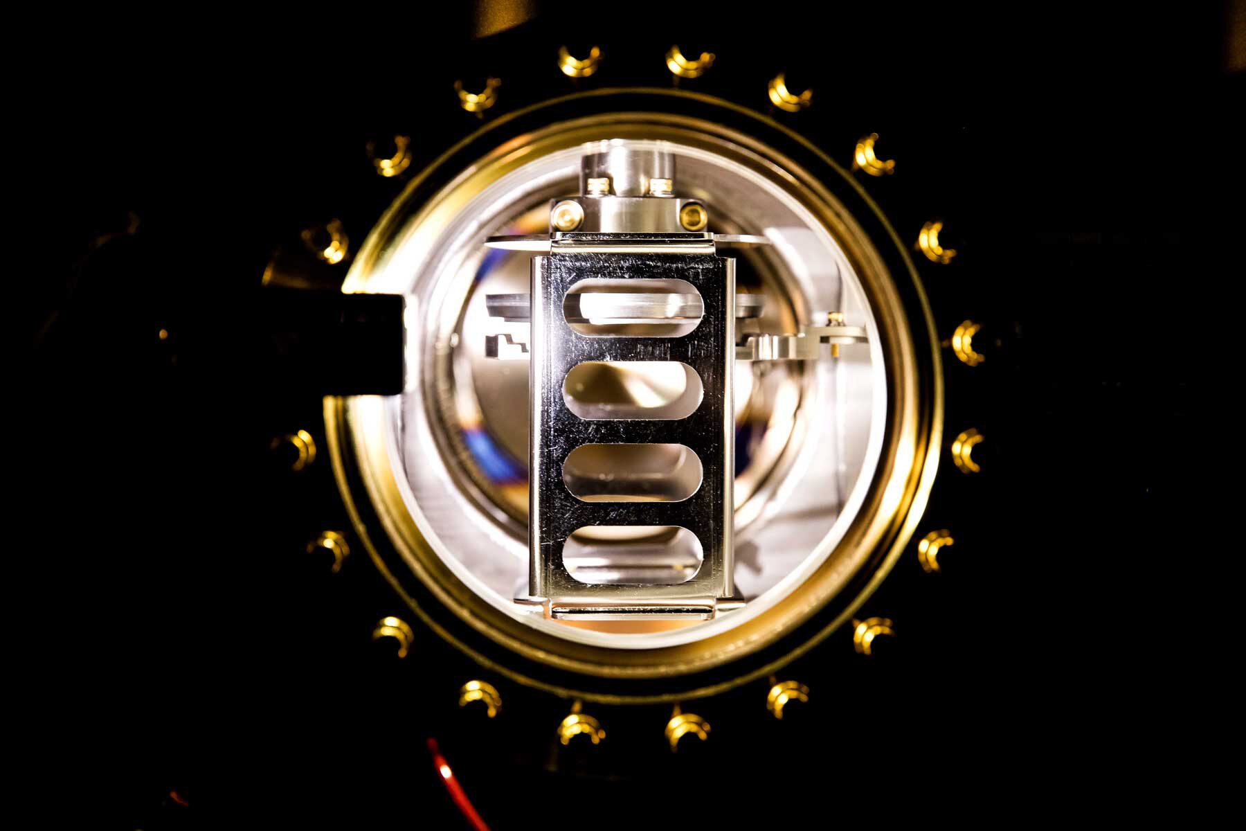 Looking down a tube toward brightly lit components shining silver, surrounded by a gold-tone ring secured with 20 bolts.
