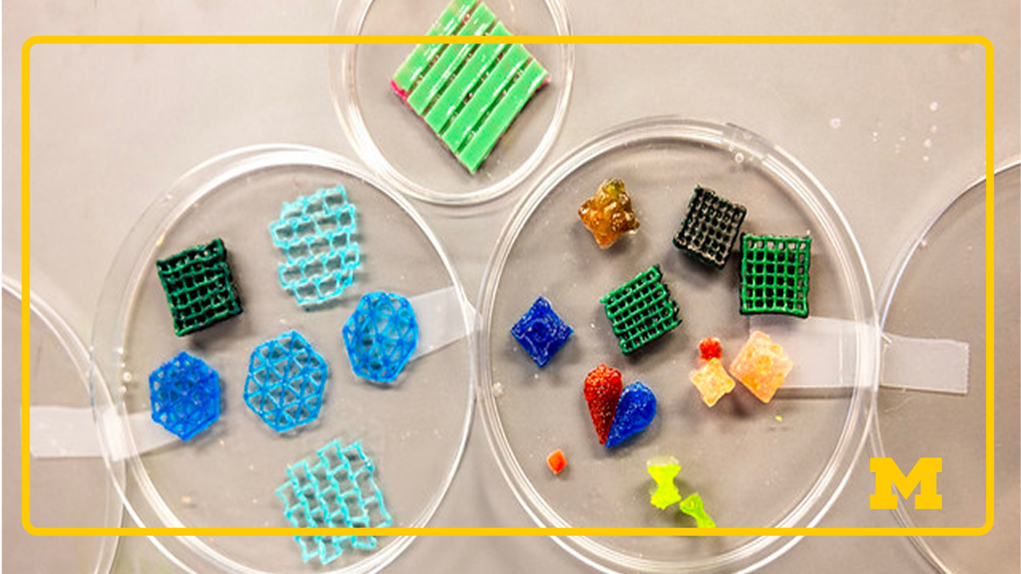 Colorful 3D printed geometric shapes in petri dishes, including grids, cubes, and hearts, arranged on a laboratory surface.