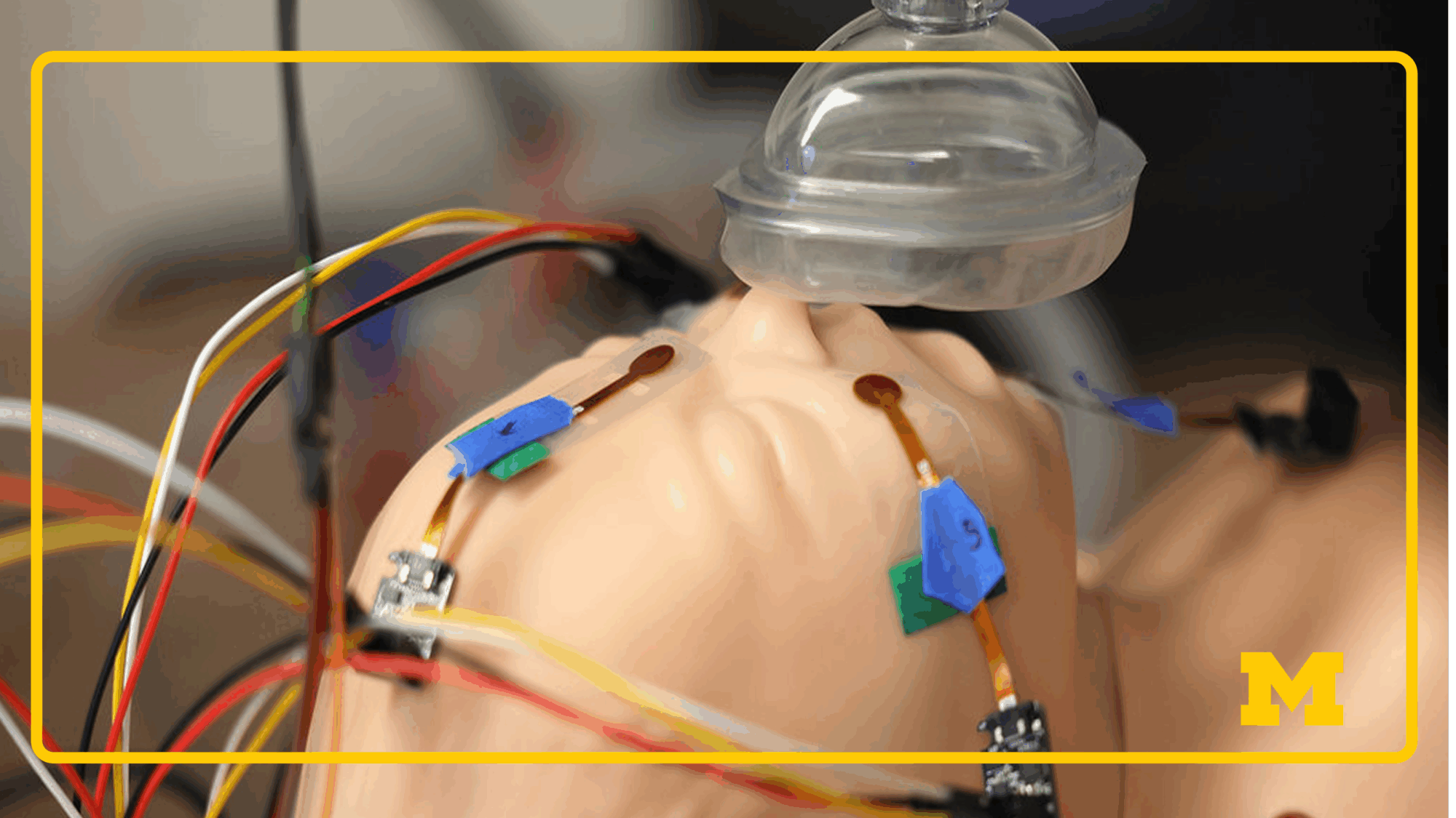 A medical training mannequin with facial sensors and tangled wires, wearing a transparent mask for simulated respiration research.
