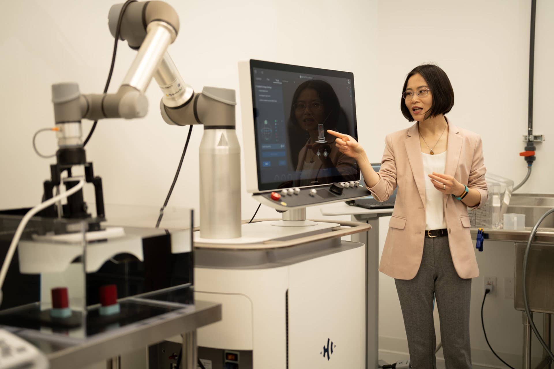 Person in professional attire interacting with a robotic medical system and touchscreen monitor in laboratory or clinical setting.