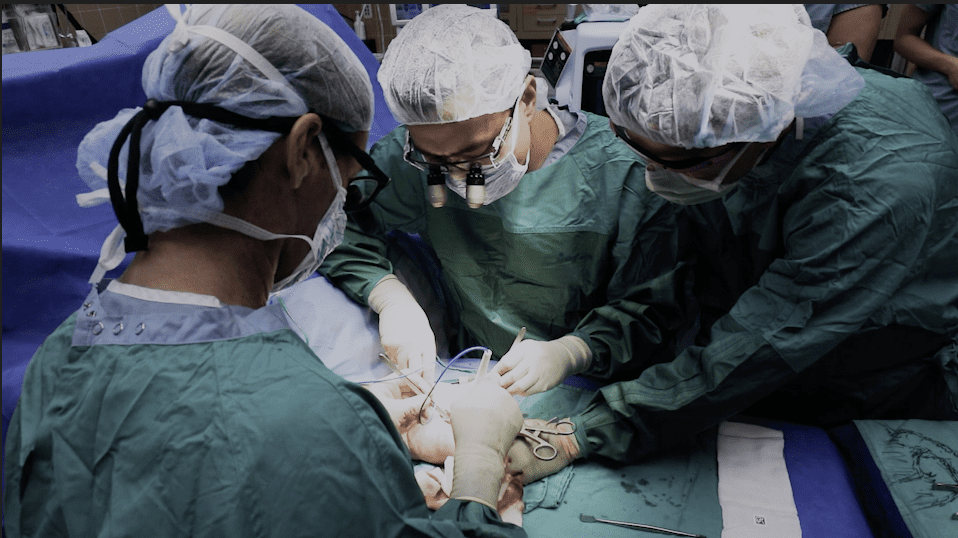 Medical team in surgical gowns and caps perform an operation, using instruments and working collaboratively on a patient’s procedure.