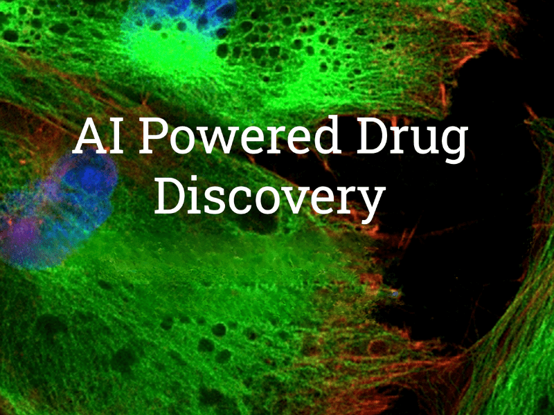 AI Powered Drug Discovery A laboratory featuring a large gray Yokogawa-branded scientific instrument next to a glass-enclosed automated robotic device on a metal frame. The setup is in a dark room with overhead lighting and computer equipment visible on a desk in the background.