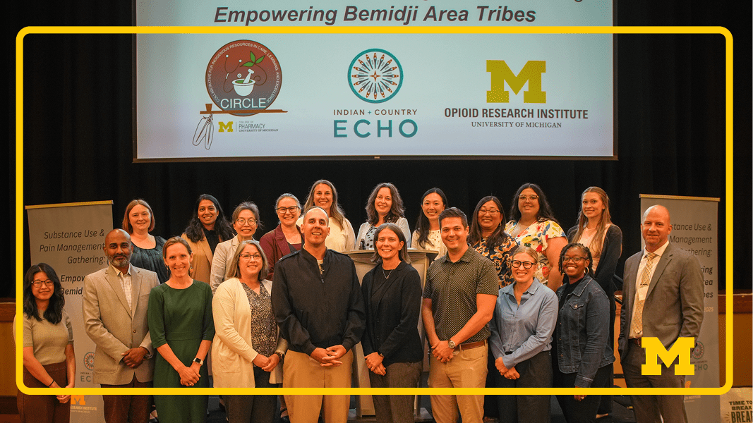 UM Pharmacy collaboration with Tribal Community Group photo on a stage at a conference, with about 15–20 people standing in two rows beneath a banner reading “Empowering Bemidji Area Tribes” and logos for Circle, Indian + Country ECHO, and the University of Michigan Opioid Research Institute, flanked by podium signs about substance use and pain management.