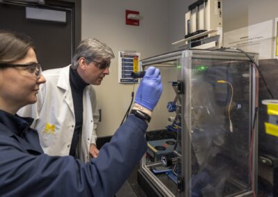 Fjorela Xhyliu (first from left) and Joerg Lahann (second from left) use a green laser to check that the electrohydrodynamic jetting process is working.