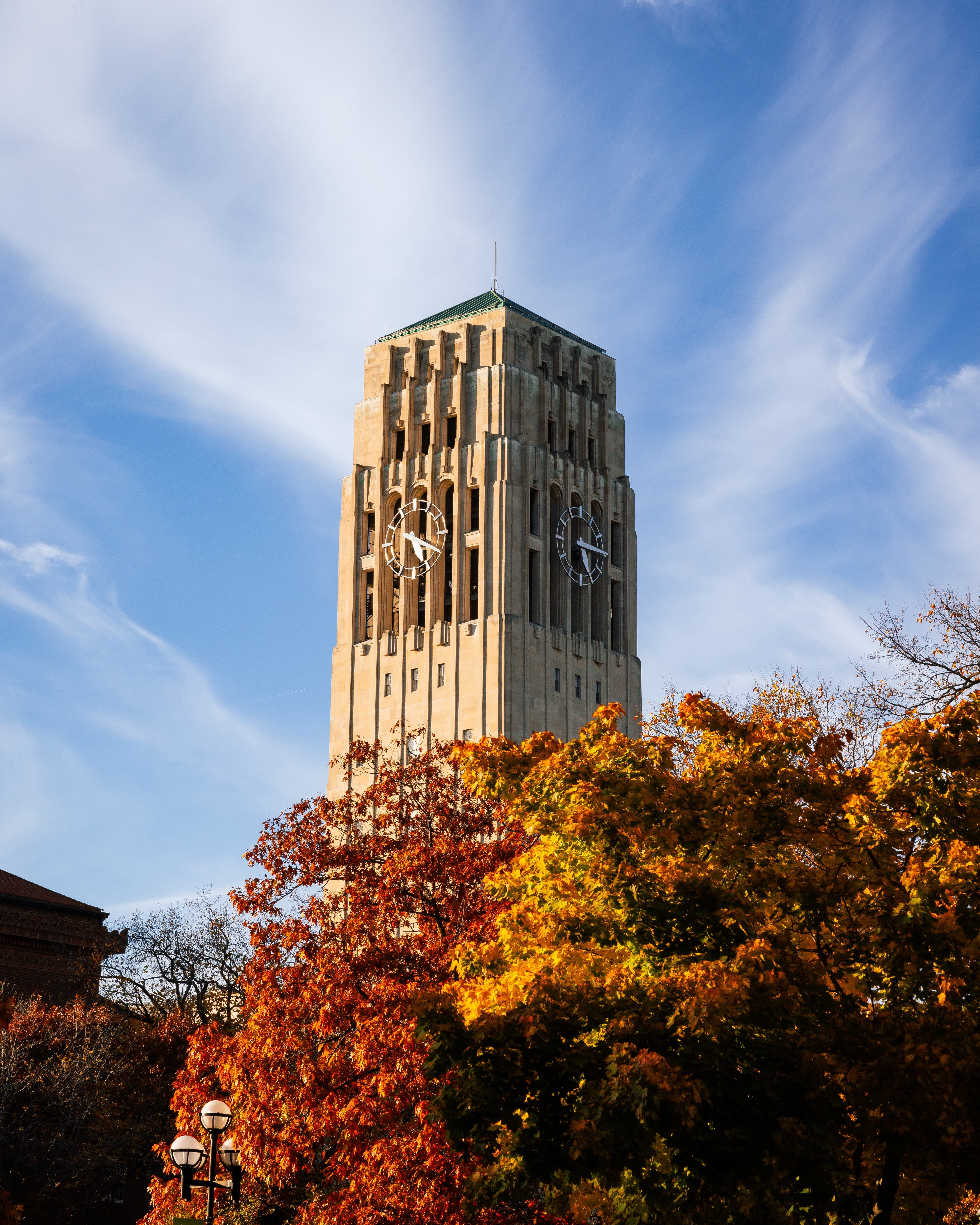 MCOMMONS Burton Memorial Tower stands against a blue sky with long wispy white clouds on a Fall evening.