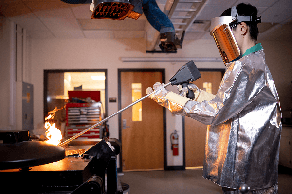 Eng_foundry Researcher in reflective protective gear tests fire behavior using a long instrument.